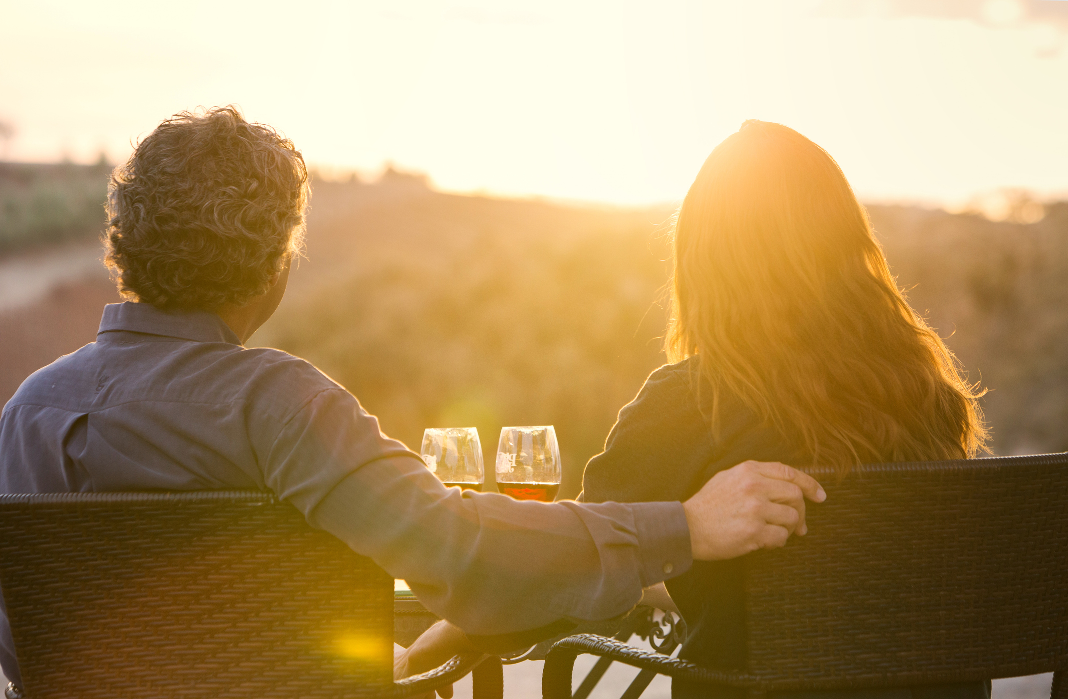 Man and Woman Sitting with Wine Glasses Overlooking Vinyard at Sunset Canadians living in United States