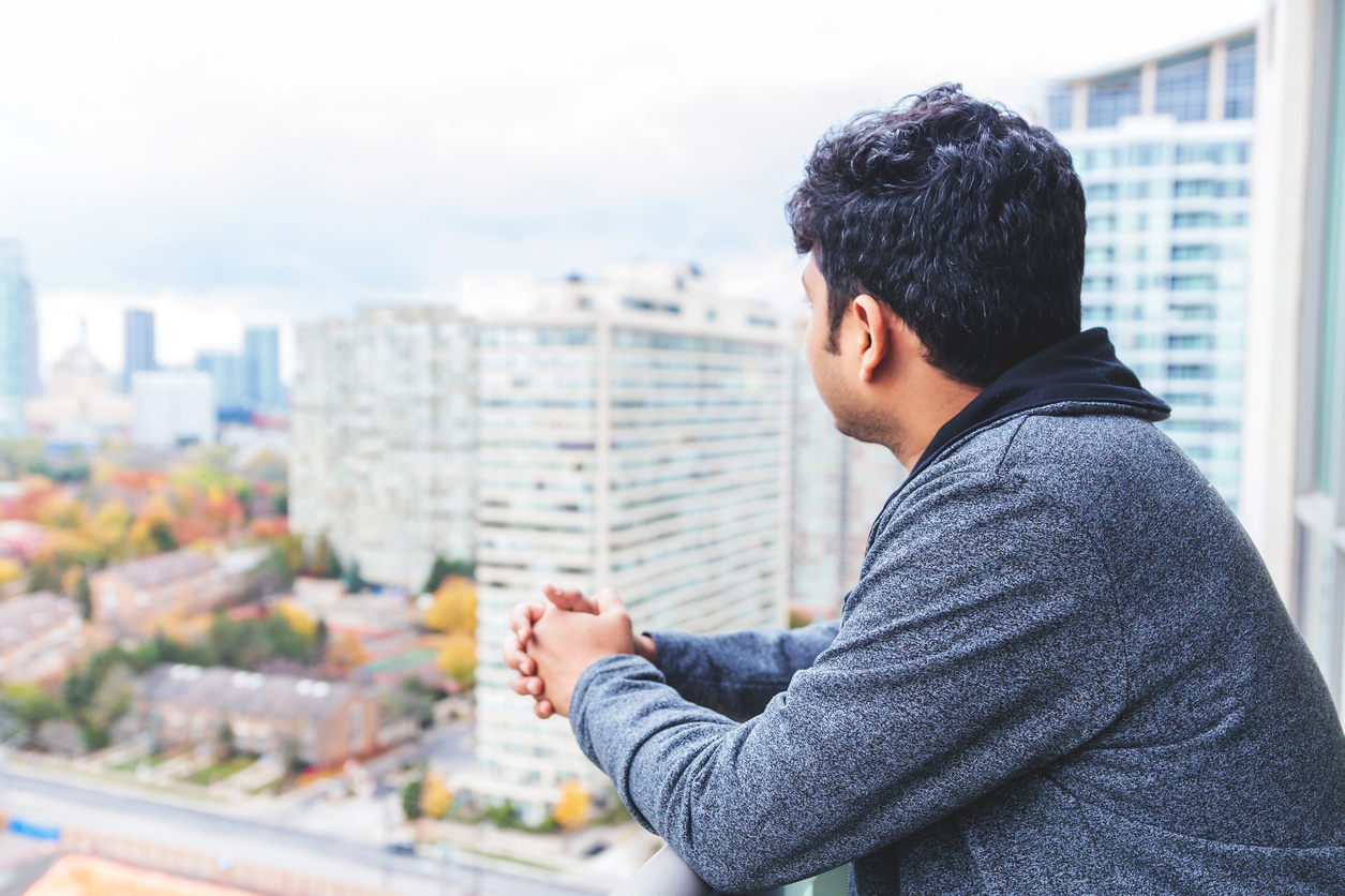 Young man newly immigrated to Canada admiring views from his apartment balcony of a highrise Roth IRAs and Moving to Canada