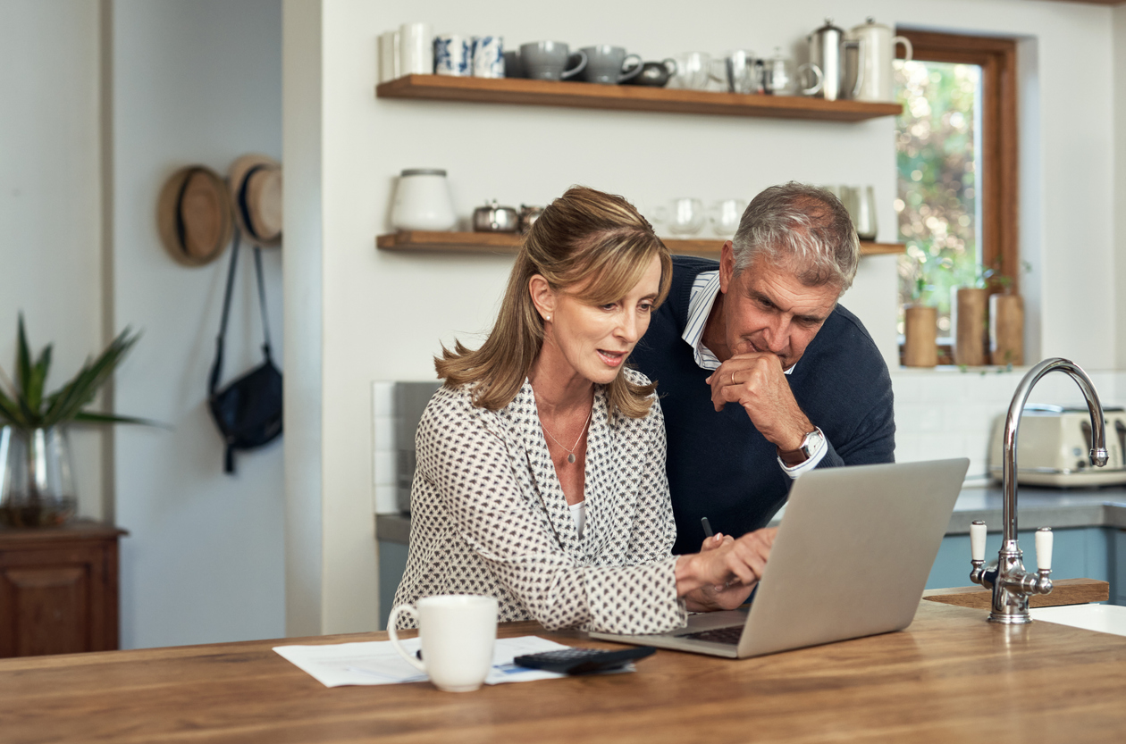 A senior couple planning their finance and paying bills while using a laptop at home. A mature man and woman going through paperwork and working online with a computer couples social security tax